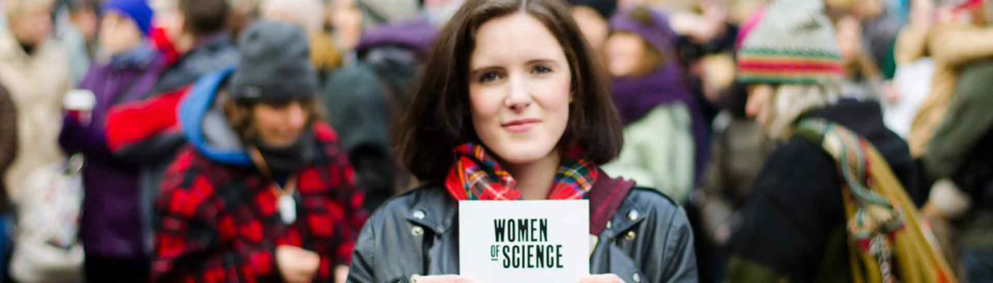 Woman holding up card that reads 'Women of Science'.