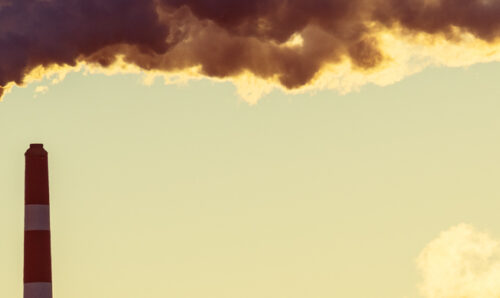 Smoke and steam billows from power plant smoke stacks in early morning light.