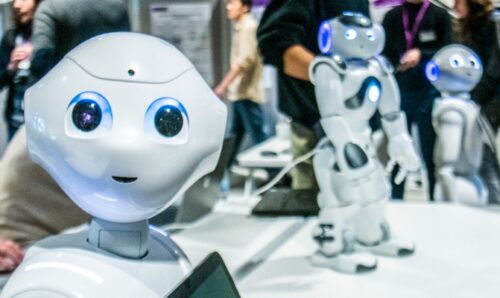 A robot in the foreground looks into the camera while two more in the background look on.