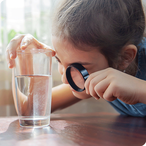 Child viewing a glass of water through a magnifying glass